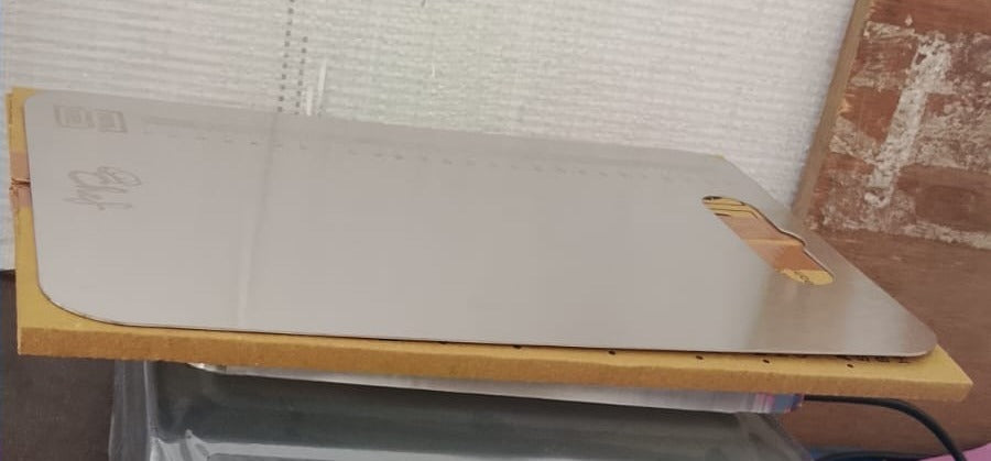 A stainless steel cutting board with ruler markings and 'Chef' engraving, resting on a brown surface.
