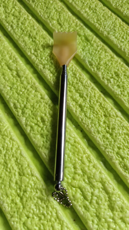 A silver telescoping back scratcher with a yellow hand-shaped head resting on a textured green surface.
