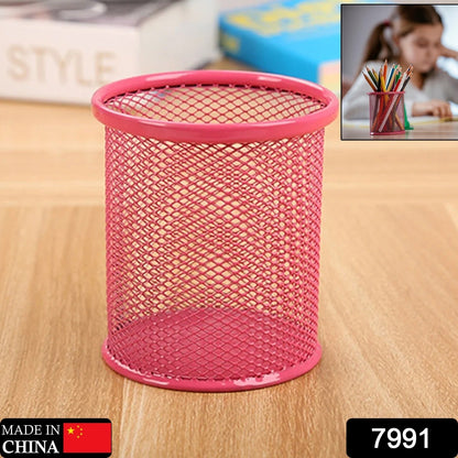 A pink metal mesh pen holder sits on a wooden surface with a blurred background showing a child drawing.