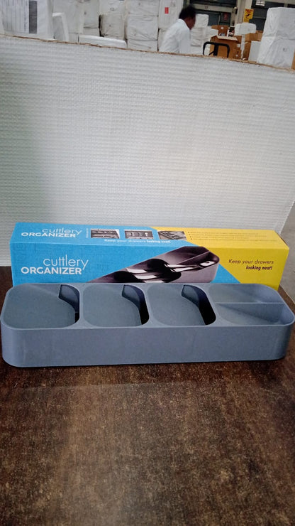 A gray plastic cutlery organizer sits on a wooden surface in front of its blue and yellow retail packaging.