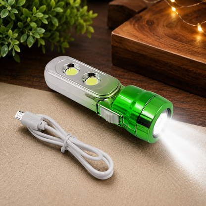 A green and silver torchlight with a white USB cable on a light brown surface with green plants and fairy lights in the