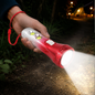 A hand holds a red and silver LED torchlight illuminating a dark path with a bright beam.