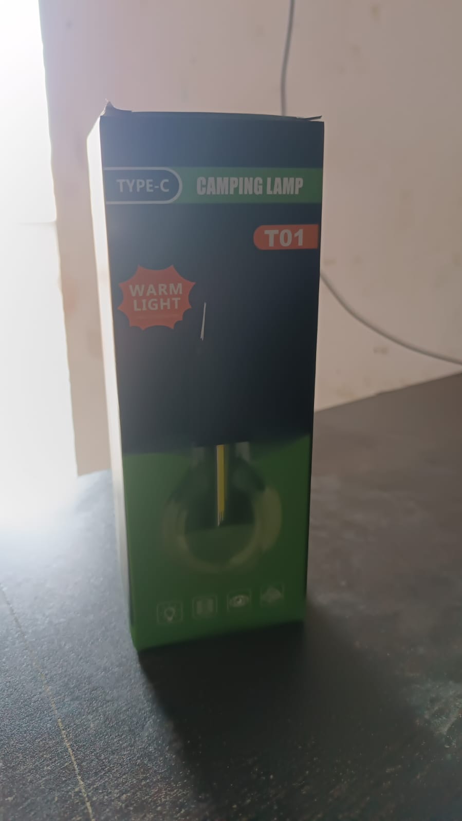 A green and black box for a camping lamp is shown on a dark surface.