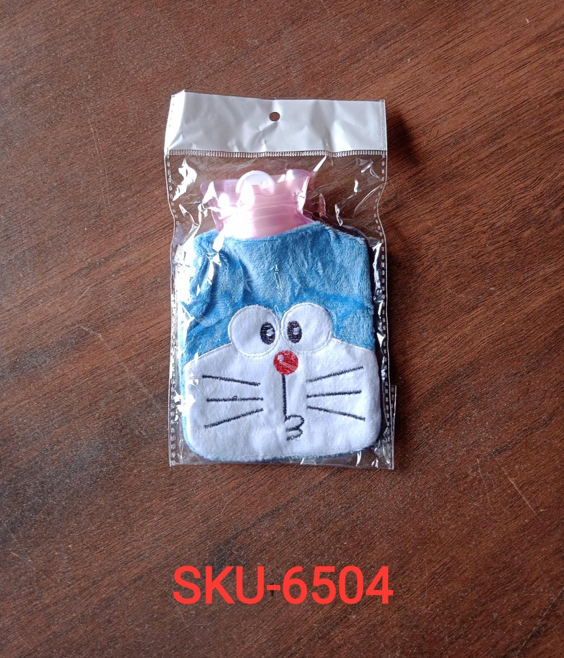 Blue Doraemon plush hot water bag with a pink stopper, sealed in clear plastic packaging on a wooden surface.