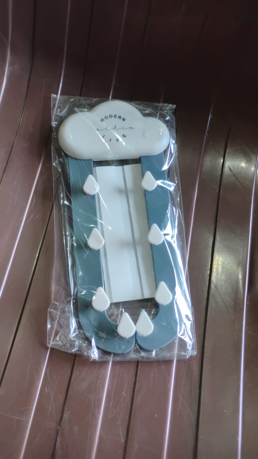 The cloud-shaped holder with blue rain-like arms and white raindrop hooks, packaged in clear plastic on a brown ribbed