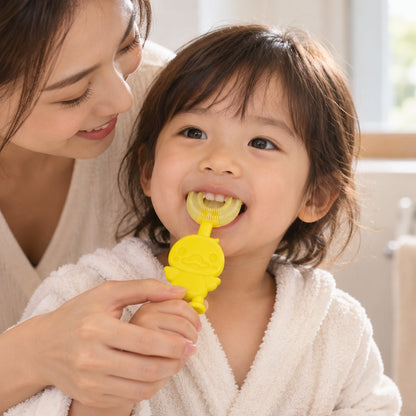 A smiling adult helps a young child brush their teeth with a yellow duck-shaped U-shaped toothbrush.