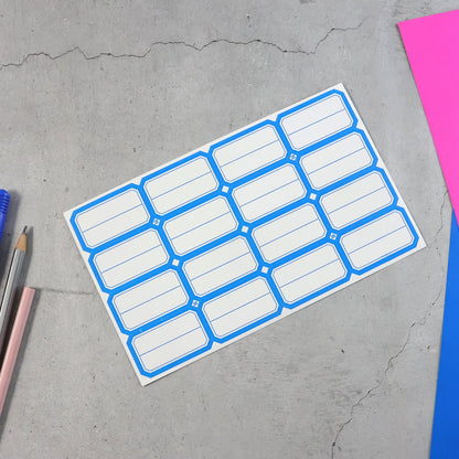 A sheet of blue-bordered label stickers is placed on a gray surface, next to colorful pens and paper.
