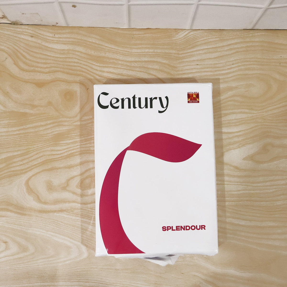 A white ream of Century Splendour paper with a large red C-shaped design on a light wooden surface.