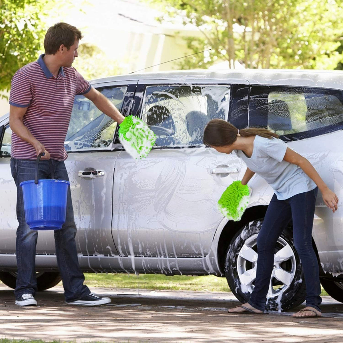 A man and a child wash a silver car with bright green microfiber gloves, surrounded by soap suds.