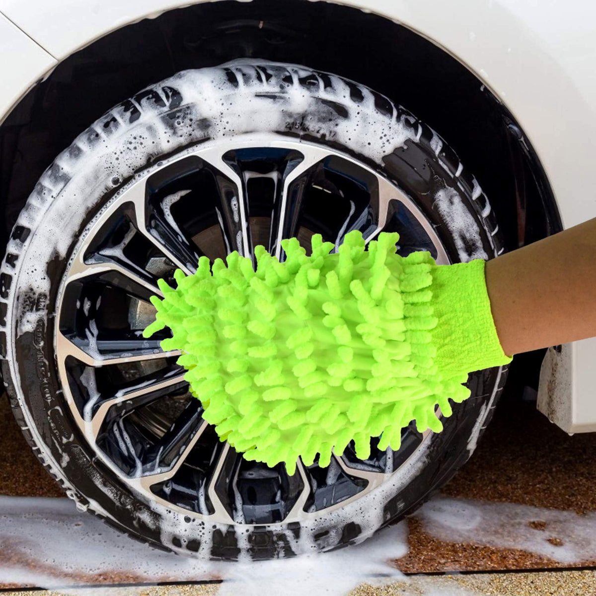 A hand wearing a bright green microfiber glove cleans a car wheel with black spokes and white suds.