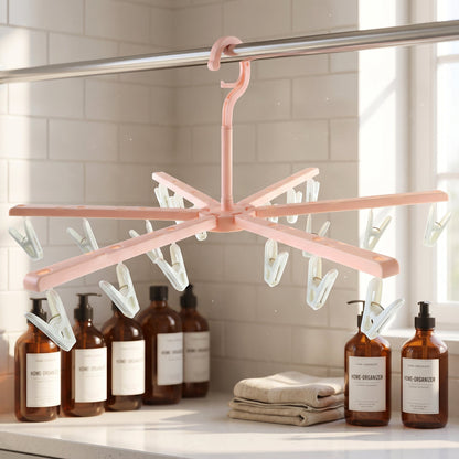 A pink plastic foldable clothes drying rack with white clips hangs above brown bottles and folded towels on a counter.
