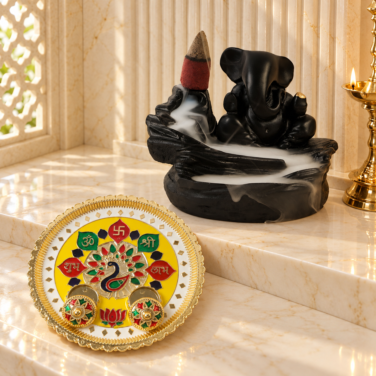 A black Ganesha backflow incense burner with smoke and a yellow and gold puja thali with peacock design.