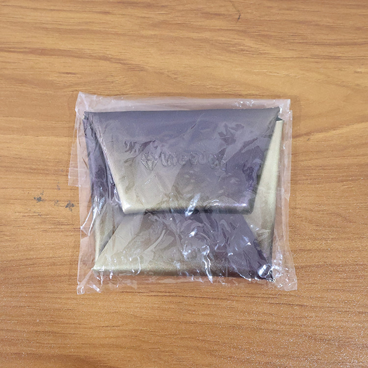 The iridescent purple and gold coin pouch is sealed in clear plastic packaging on a wooden surface.