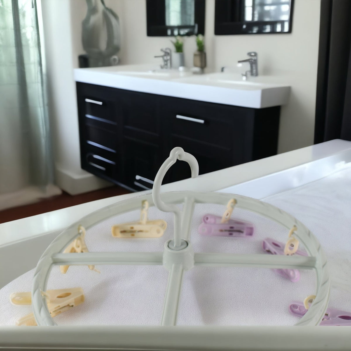 A light blue circular drying rack with purple and yellow clips rests on a white surface in a bathroom setting.