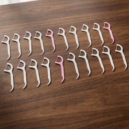 Twenty pink and white dental floss picks arranged in rows on a wooden surface.