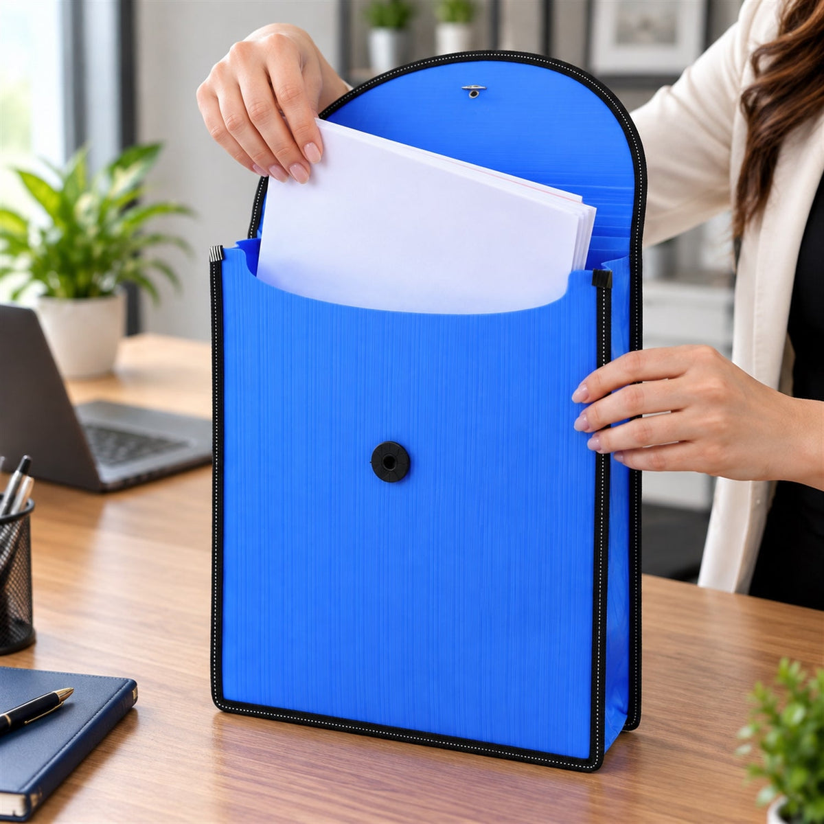 Hands inserting white papers into the open blue plastic folder with a black elastic closure on a wooden office desk.