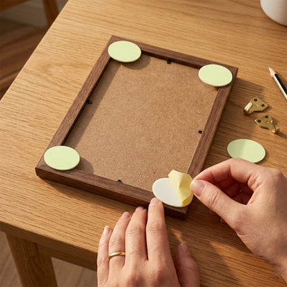 Hands applying a yellow oval pad to the back of a wooden picture frame, with other pads already in place.