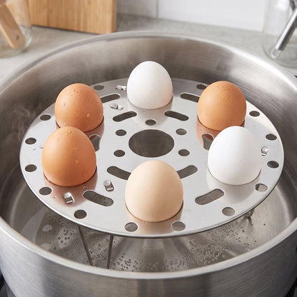 A close-up of a stainless steel steamer rack in a pot, holding six eggs of various brown and white shades, with bubbling