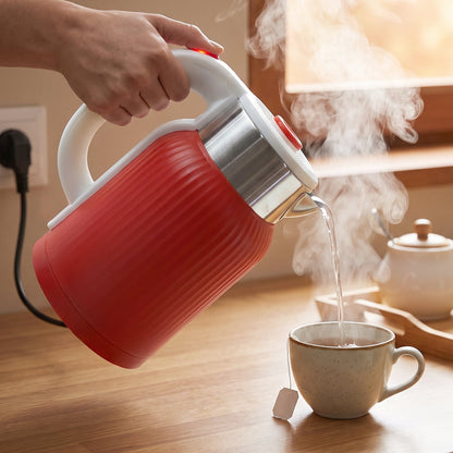 A person's hand holds a red ribbed electric kettle, pouring steaming water into a light-colored teacup on a wooden surface.
