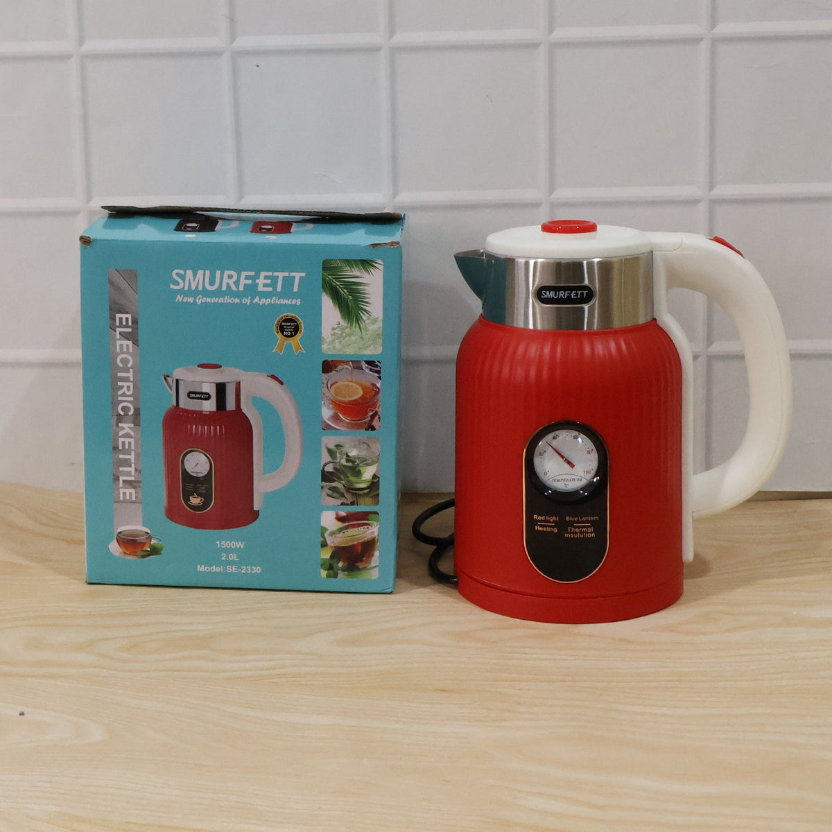 A red ribbed electric kettle with a temperature gauge is next to its blue and white product box on a light wooden surface.