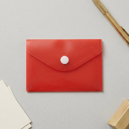 A red plastic document folder envelope with a white button closure is placed on a grey surface next to a gold pen and small