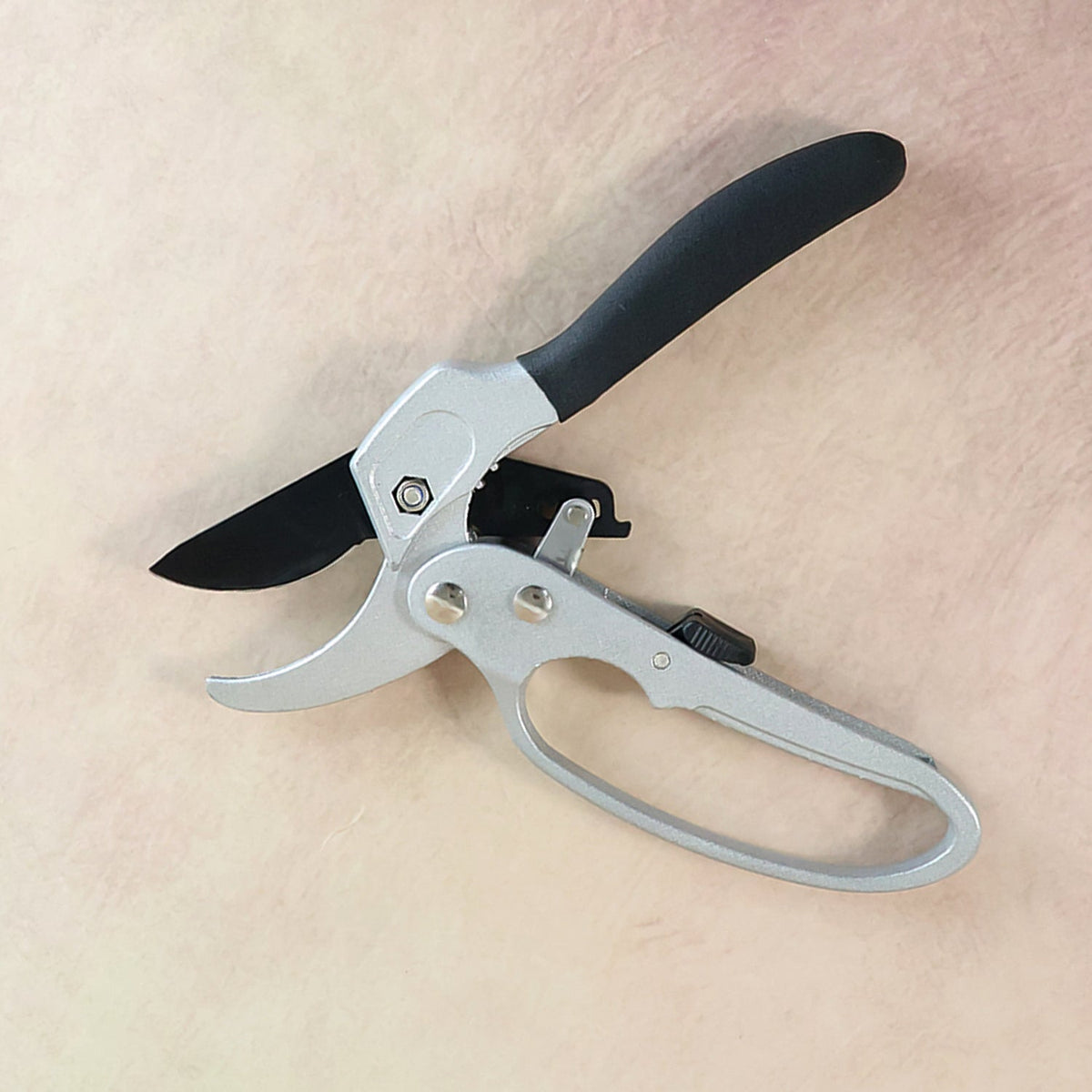 Silver and black pruning shears with an ergonomic handle and black blade on a light brown background.