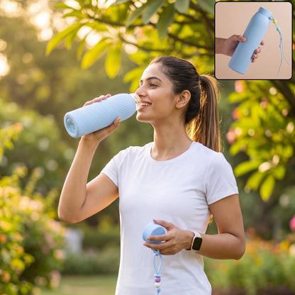 A woman in a white t-shirt drinks from a light blue ribbed glass water bottle in a park setting.