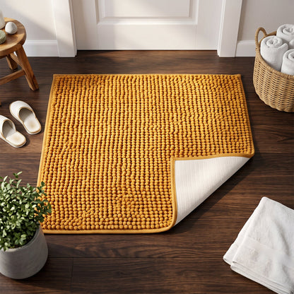 A mustard yellow bobble mat with a turned-up corner revealing its white backing, on a wooden floor with home decor.
