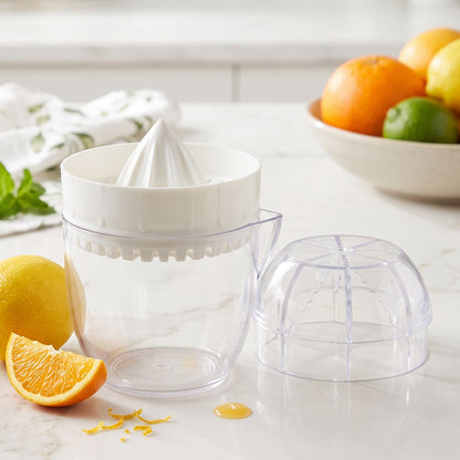 A white and clear plastic citrus squeezer, disassembled, on a marble counter with lemons, orange slices, and mint leaves.