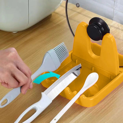 A hand placing a gray silicone brush onto a yellow plastic lid and spoon rest, next to a knife and white spoon.