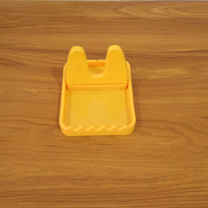 An empty yellow plastic lid and spoon rest centered on a light brown wooden table.