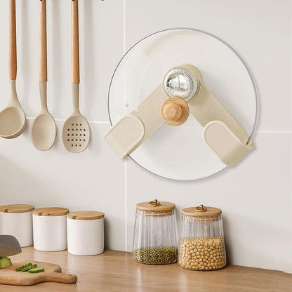 A cream pot lid holder with a wooden knob and chrome center holds a glass lid on a white tiled wall above kitchen counter