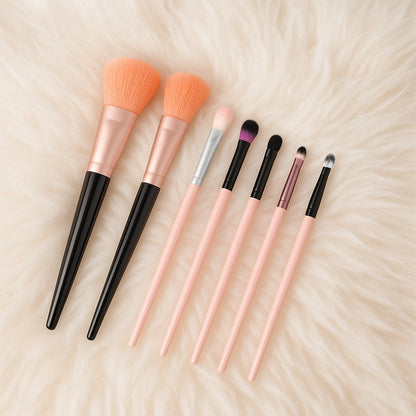 A full set of seven makeup brushes, featuring pink and black handles, rests on a soft, white, textured surface.