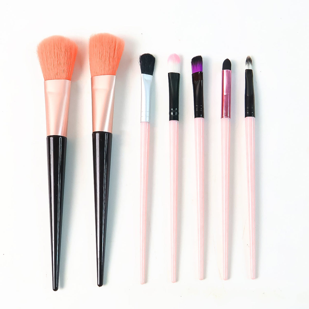 A complete set of seven makeup brushes, featuring pink and black handles, arranged neatly on a white background.