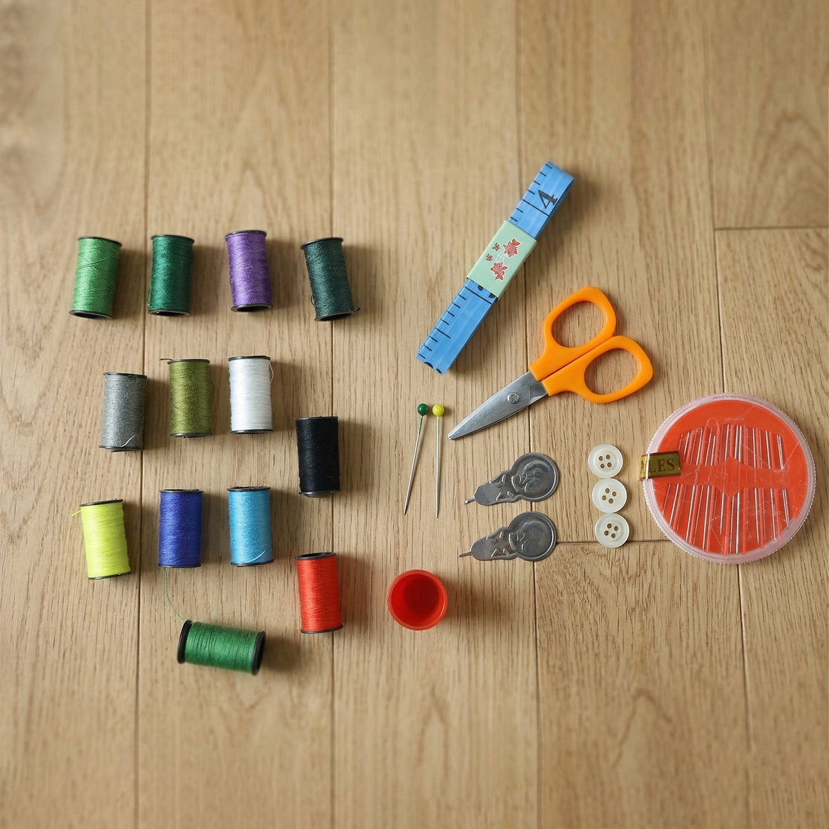Various colorful thread spools, orange scissors, a blue measuring tape, pins, buttons, and a needle case are arranged on a