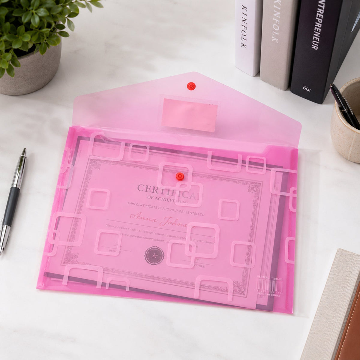 An open pink plastic document folder with a button closure, containing a certificate, on a white desk.