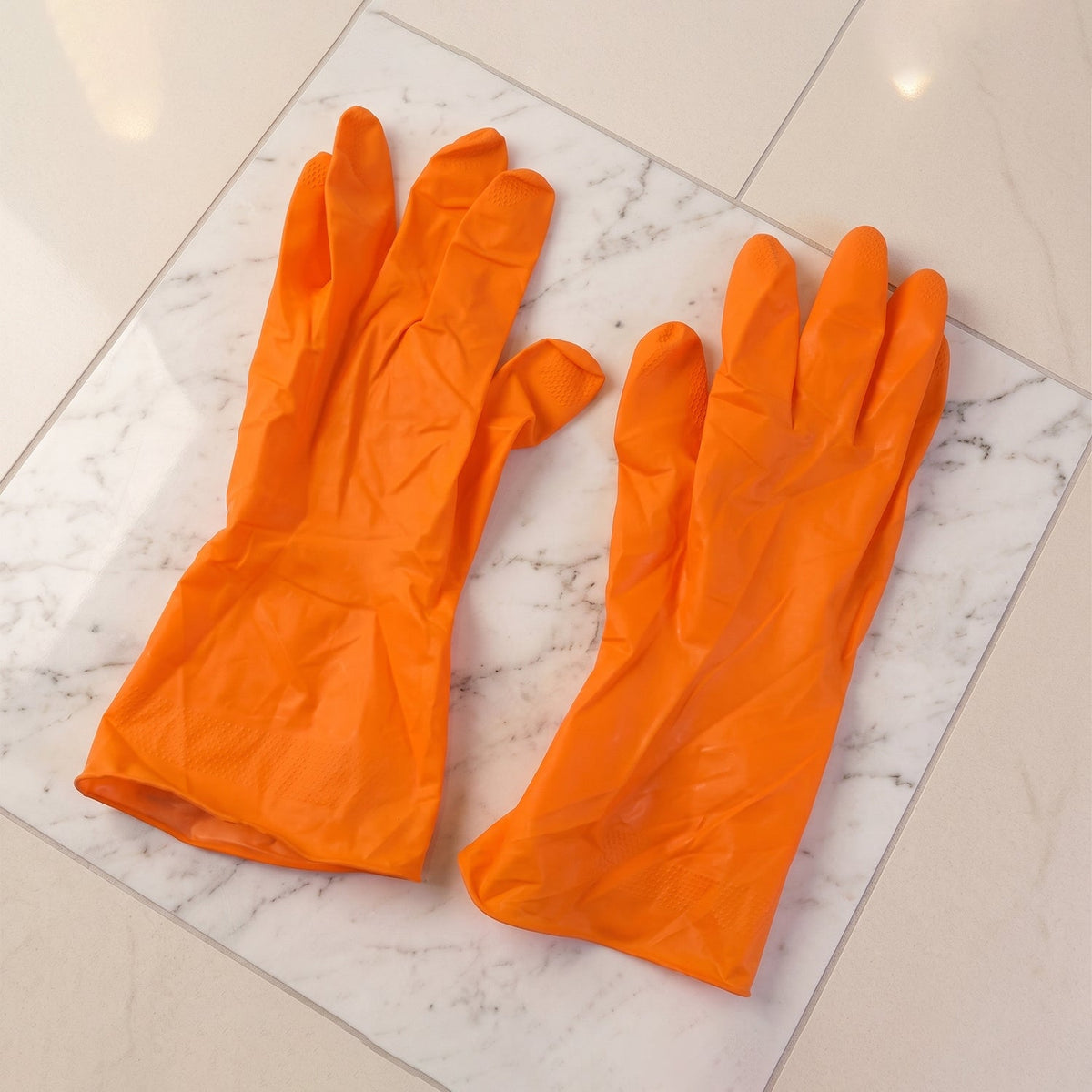Two orange rubber gloves are neatly arranged on a white and grey marble patterned surface.