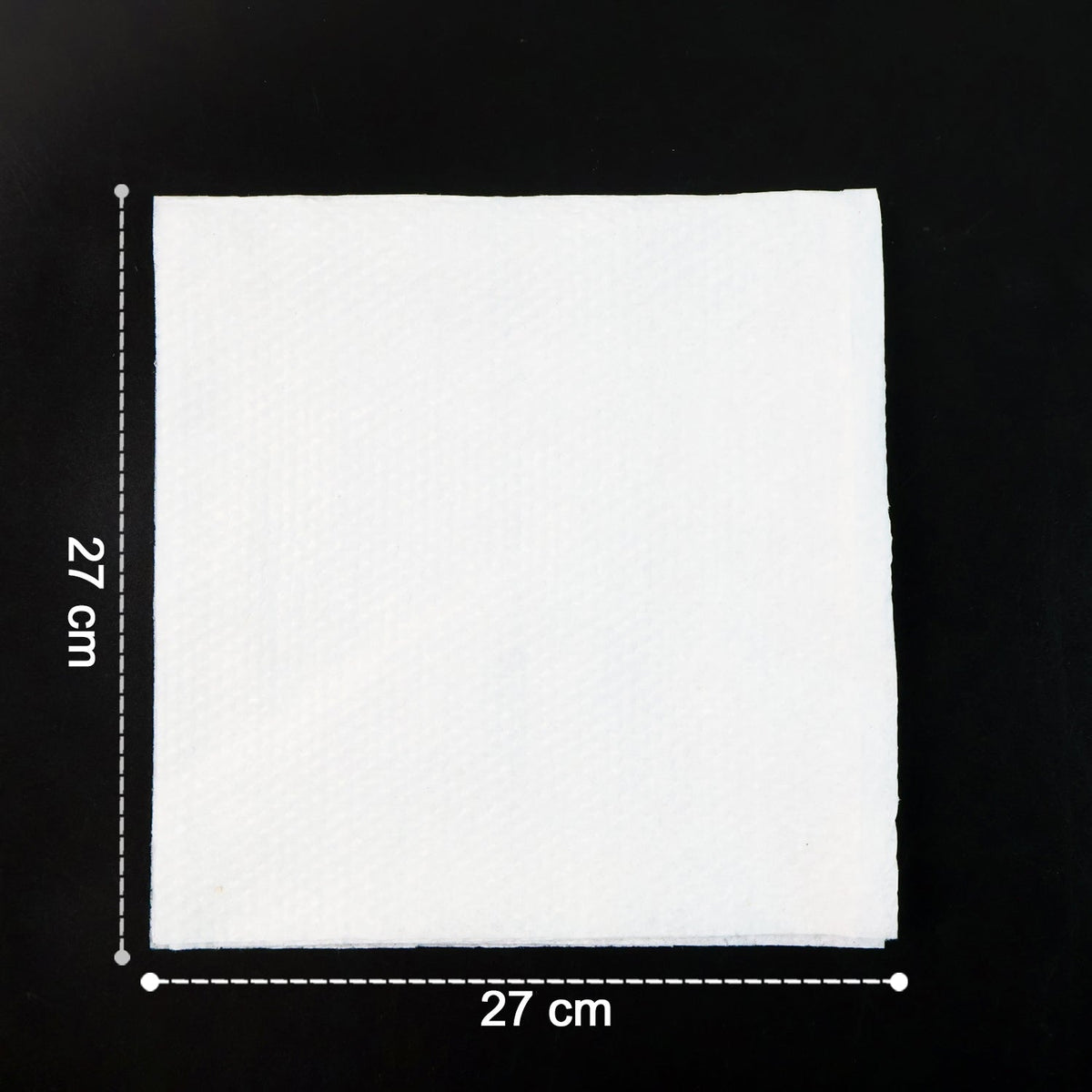 A single white paper napkin on a black surface, showing its 27 cm by 27 cm dimensions.