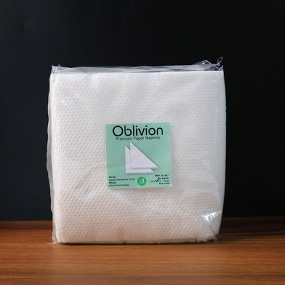 A clear plastic-wrapped package of Oblivion brand premium paper napkins on a wooden surface.