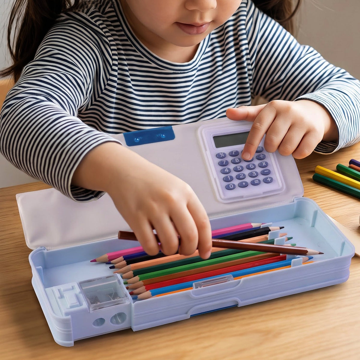 A child's hands placing colorful pencils into a light blue Avengers pencil box with an integrated calculator.
