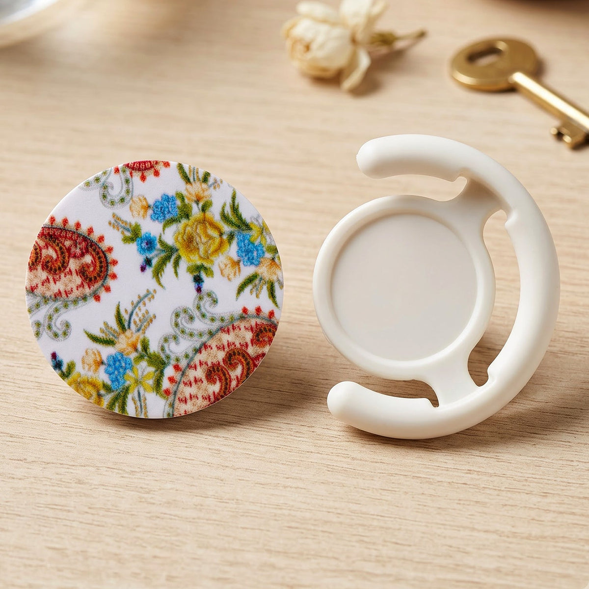 A round pop socket with a white background and colorful paisley floral pattern next to a white plastic car vent mount.