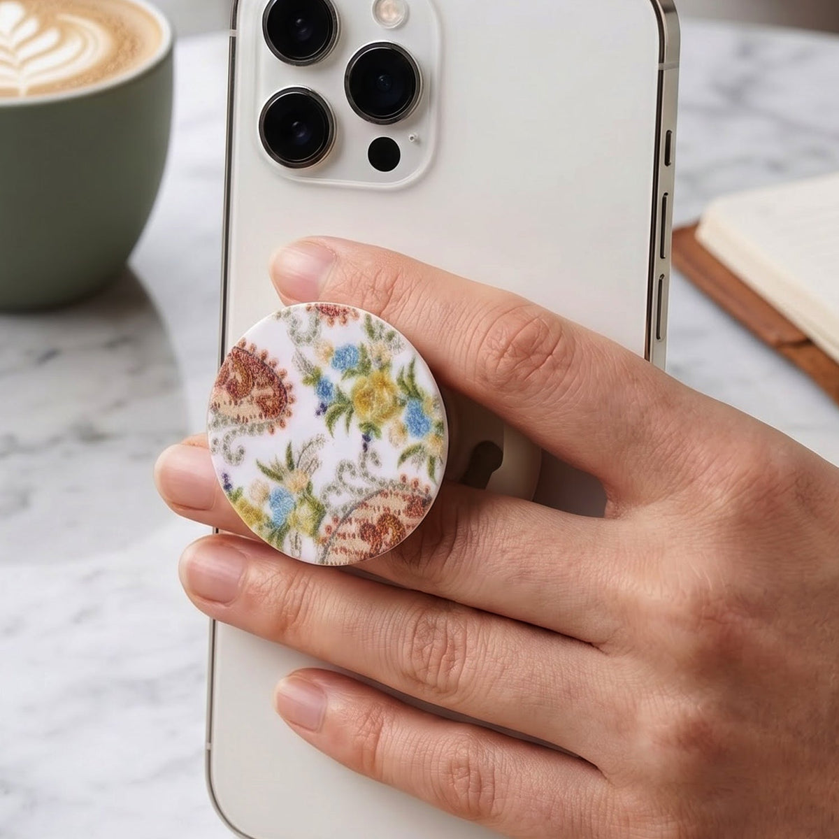 A hand holds a white smartphone with a round pop socket featuring a white background and colorful paisley floral – view 4