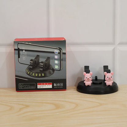 A black phone holder with two pink pig figurines next to its product box on a wooden surface.