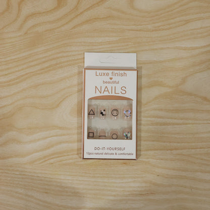 A white box of Luxe Finish Beautiful Nails, displaying 12 nude press-on nails with geometric designs and bows.