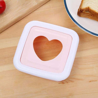 Pink and white heart-shaped sandwich cutter on a wooden surface with a plate of bread in the background.