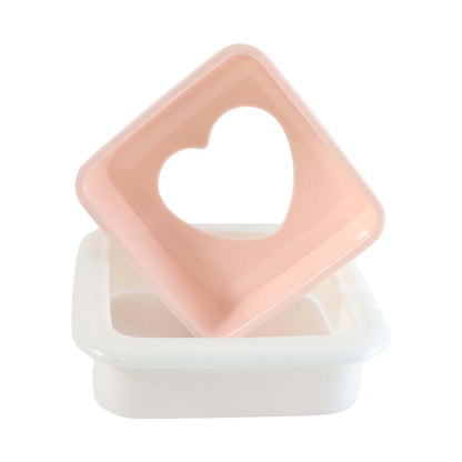 Pink heart-shaped top of a sandwich cutter resting on its white base, isolated on a white background.