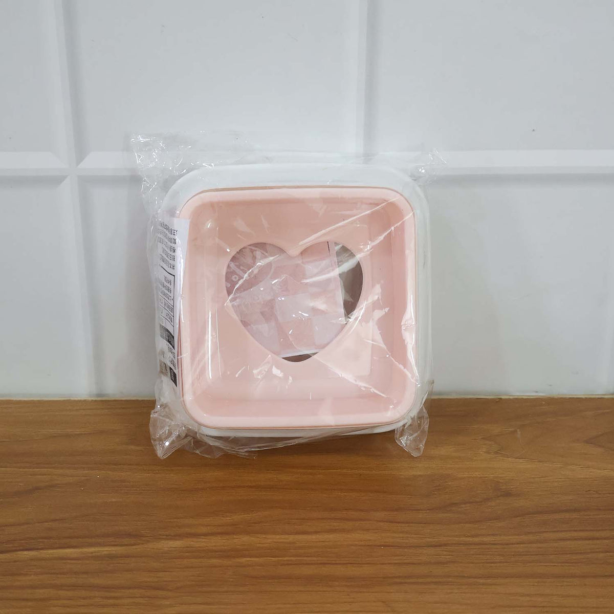 Pink and white heart-shaped sandwich cutter sealed in clear plastic packaging on a wooden surface.