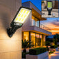 A black solar LED street light with a motion sensor is mounted on a light-colored brick wall, illuminating a house