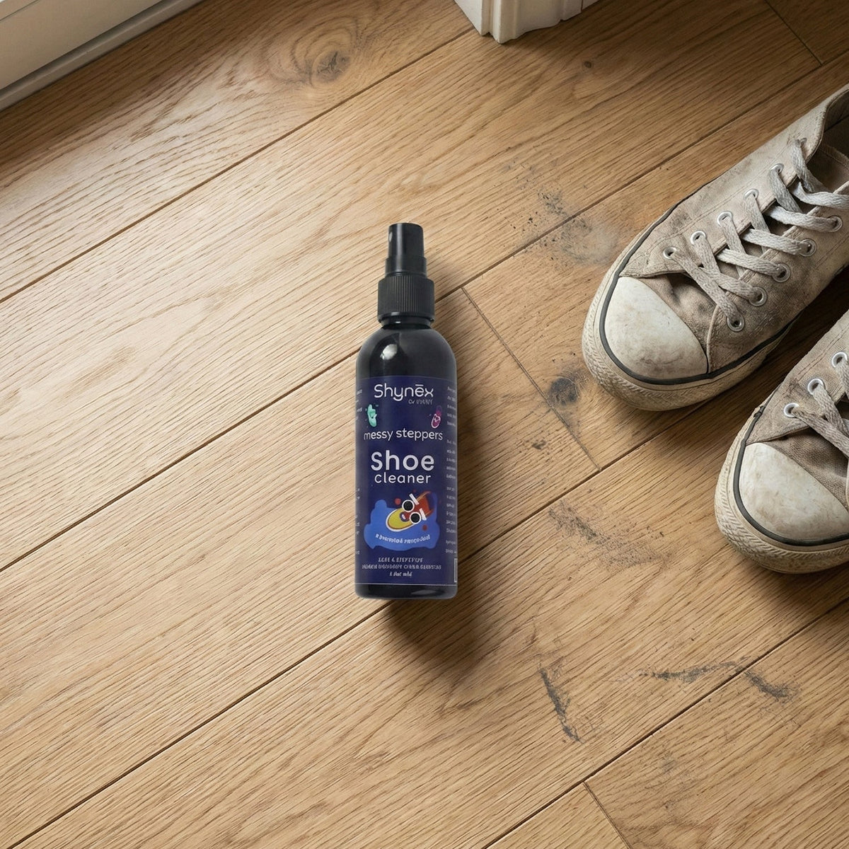 A Shynex shoe cleaner bottle stands on a wooden floor next to a pair of dirty grey canvas shoes.