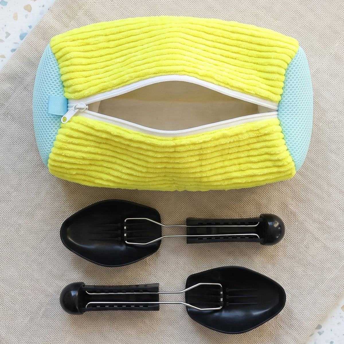 A yellow and blue shoe laundry bag with an open zipper, and two black shoe supports on a light brown fabric surface.